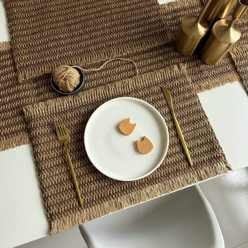 Sailorine brown woven placemats beneath a plate and gold-colored table accessories